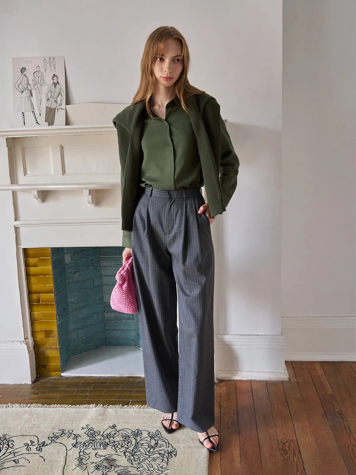 Model in ORAN trousers with olive green silk shirt, moss cardigan, and pink knitted bag indoors