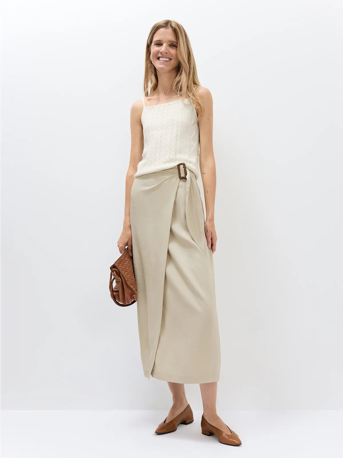 Front view of model wearing the Oatmeal acetate wrap midi skirt with a shirt and patterned heels.