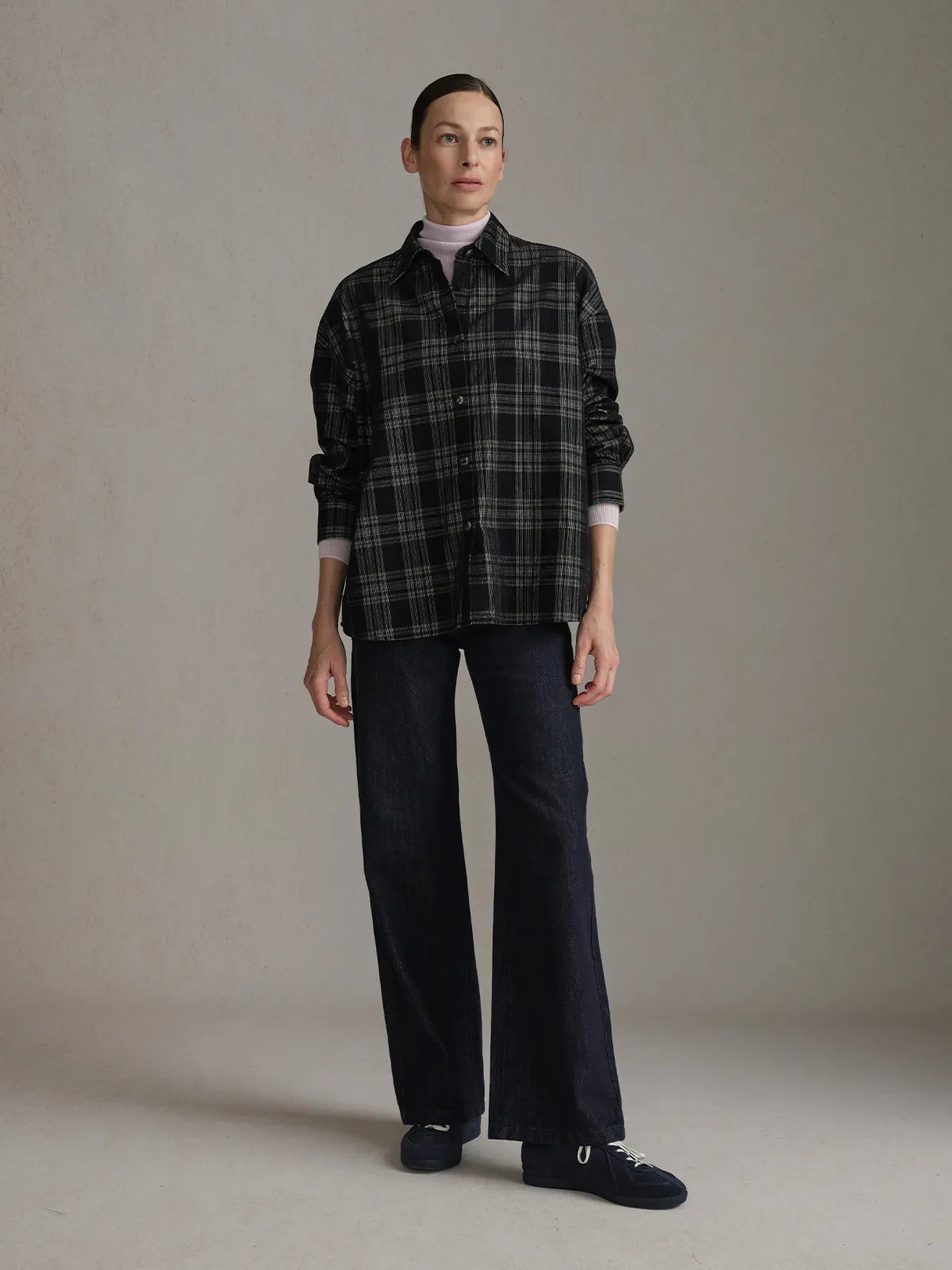 Model in CLOVER jeans with black-and-white plaid oversized shirt, minimalist sneakers