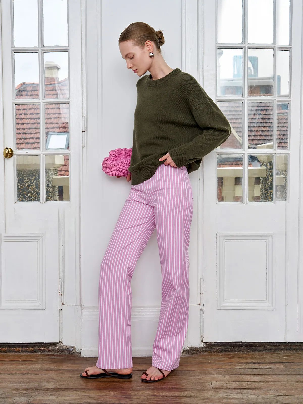 Model in olive green sweater and PINKY pink stripe jeans, holding pink crocheted clutch by French doors
