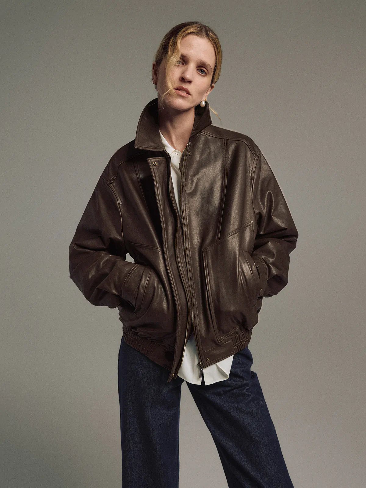 Model in a Dark Brown Italian shearling leather jacket, side view, holding a small bag.