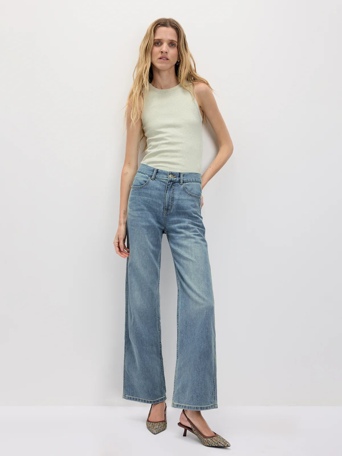 Model standing front-facing in a Light green fitted tank top with wide-leg jeans and pointed flats.