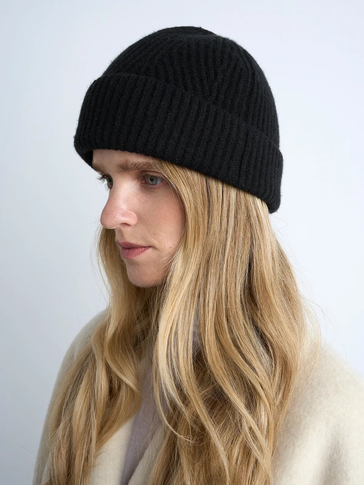 Side profile of a model wearing a black ribbed knit beanie with folded cuff.