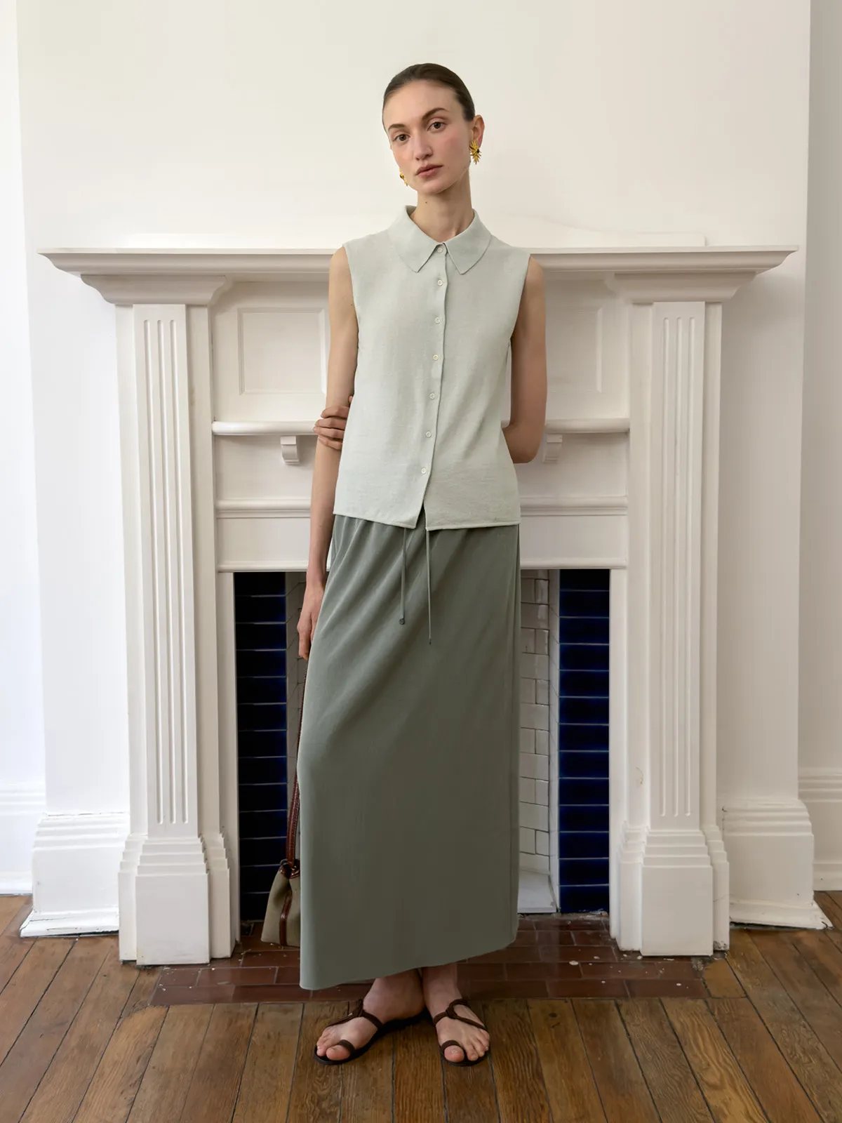 Front view model wearing KATRINA skirt with sleeveless collar shirt and leather tote by fireplace