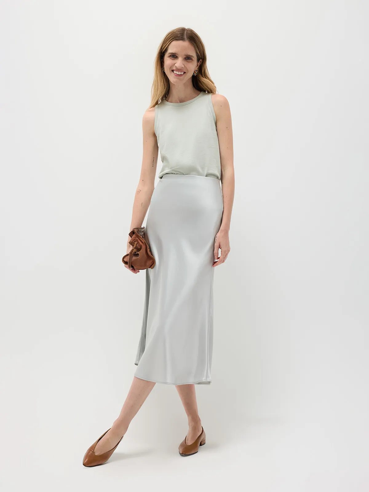 Model in sage green HOLLY tank top with light grey satin slip skirt and tan block-heel shoes