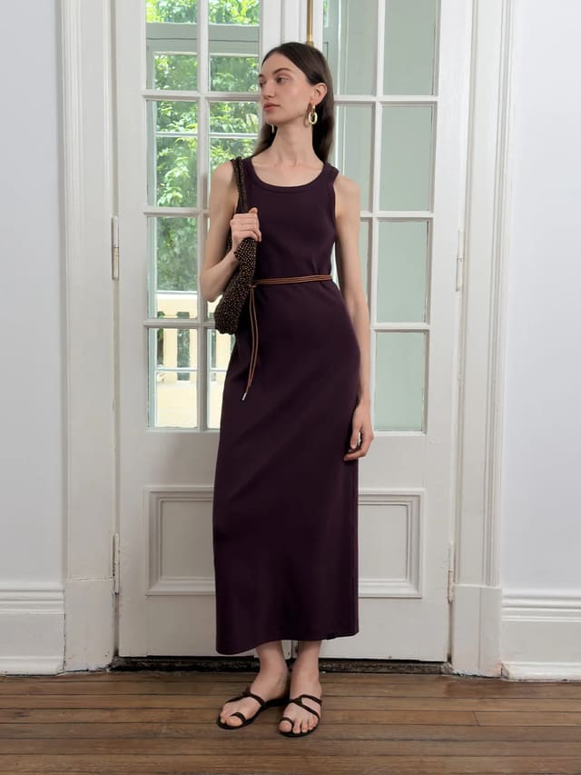 Andreatang AUBREY fitted sleeveless tank dress in deep plum, worn with brown woven belt and beaded bag, standing by white French door