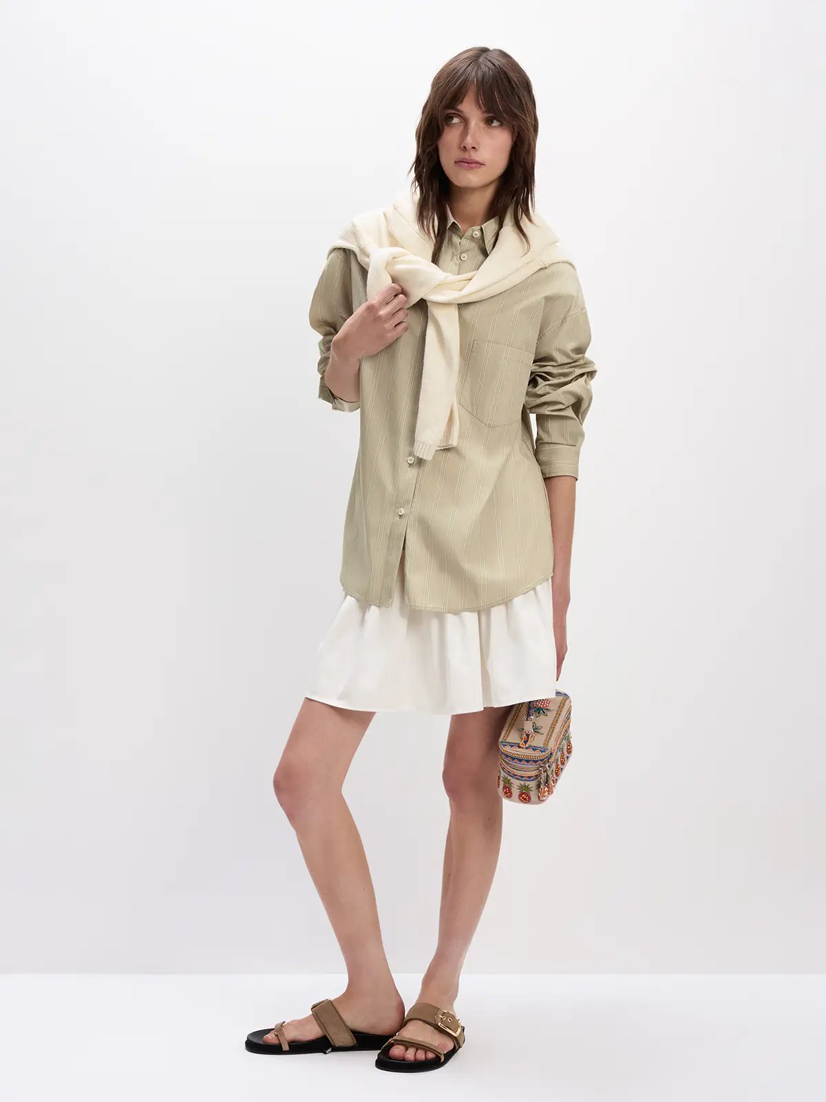 Model wearing a Khaki striped oversized cotton shirt layered over a dress with sandals and a clutch.