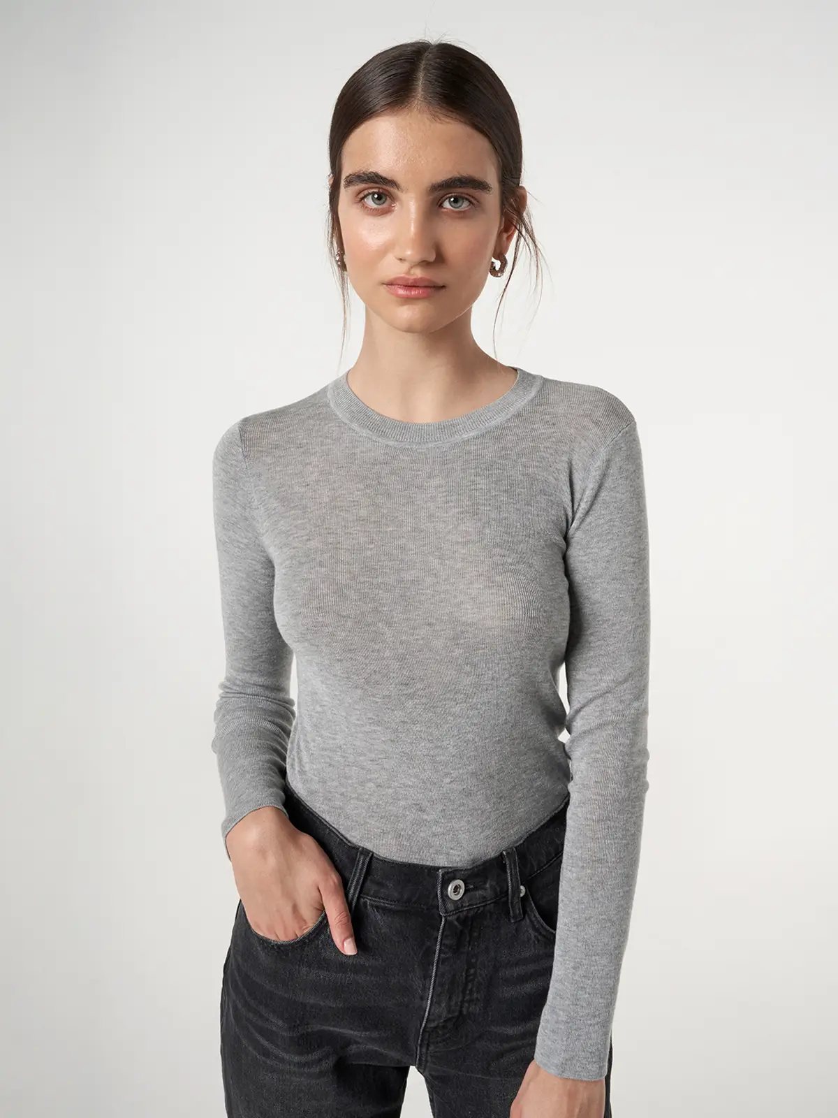 Model wearing a slim-fit, long-sleeve knit top in Light Grey with one hand in dark denim pocket.
