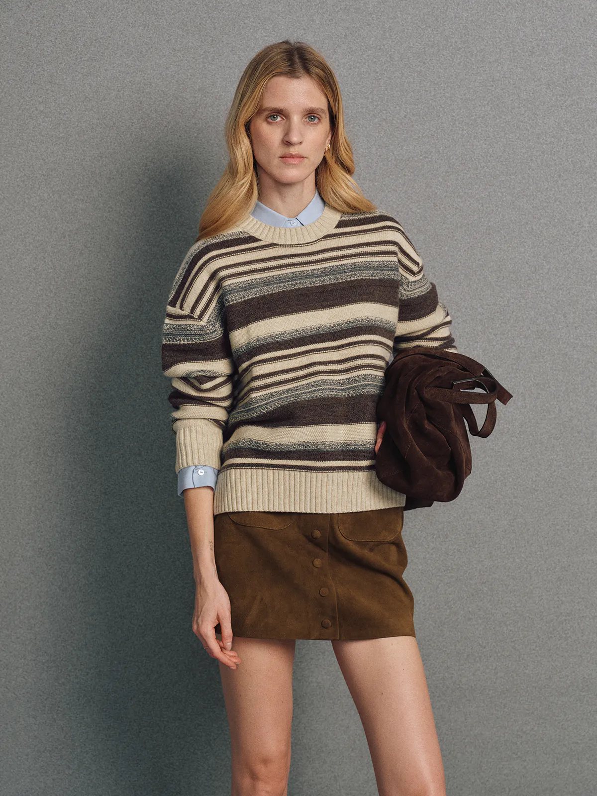 Front view of model wearing a blue irregular multicolour stripe wool cotton jumper with hands in pockets.