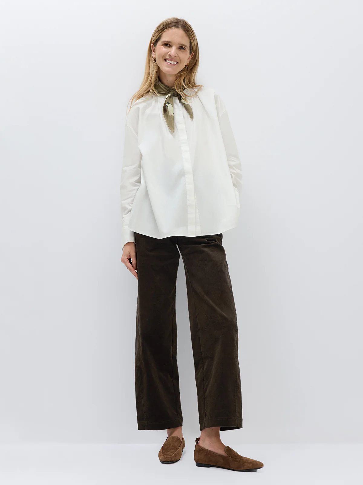 White textured blouse with a scarf tie at the neck, styled with a dark skirt and clutch in a front view.