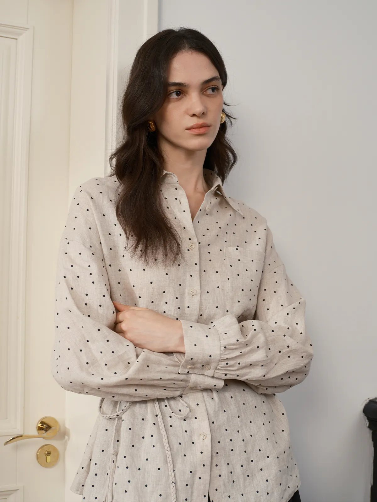 Model standing with arms crossed, wearing ODELIA polka dot linen shirt, showcasing sleeve volume and collar structure