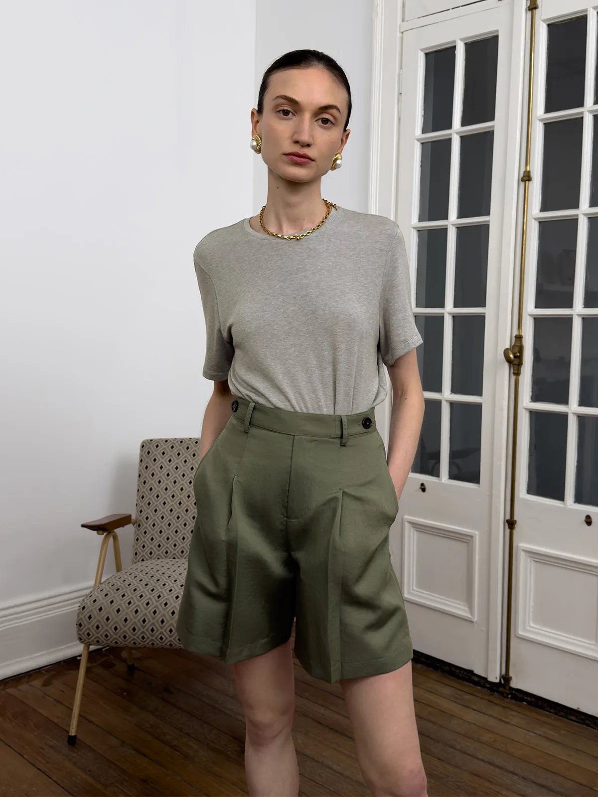 Front pose: model in gray MARY T-Shirt with olive pleated shorts, gold jewelry—Parisian chic minimalist fashion