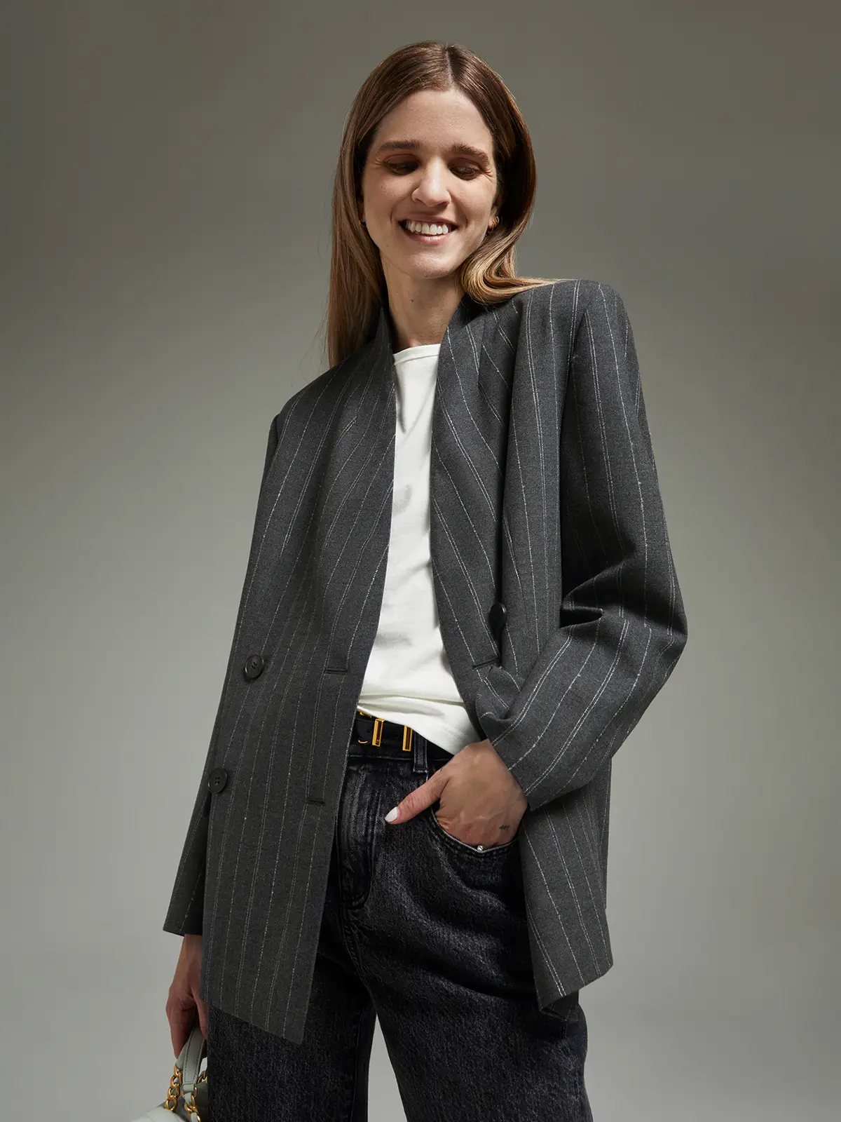 Model wearing a gray double-breasted blazer with pinstripes, hands in pockets, over a top.