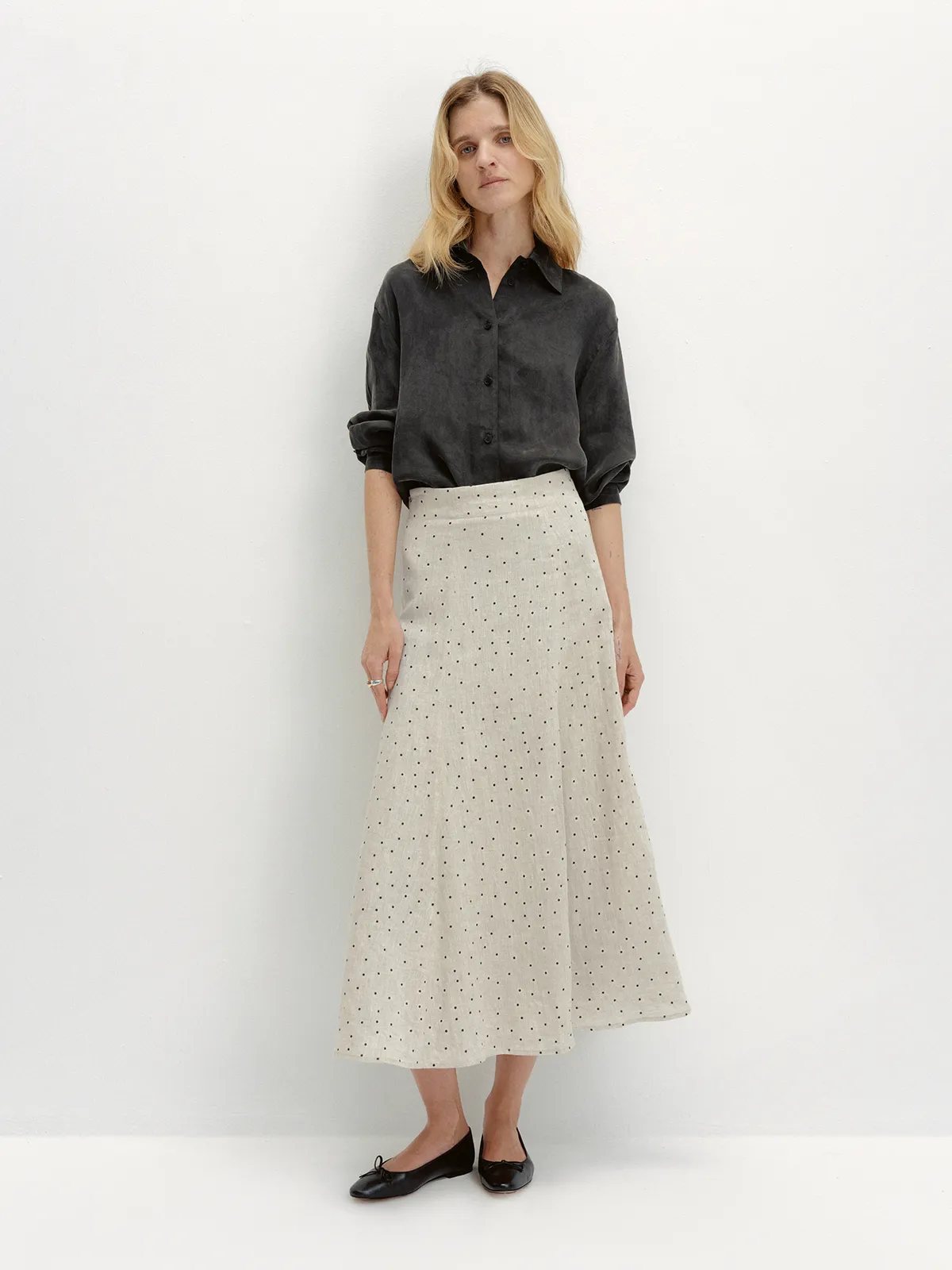 Full-body look: Model in NOBU Shirt styled with polka-dot linen midi skirt and black ballet flats