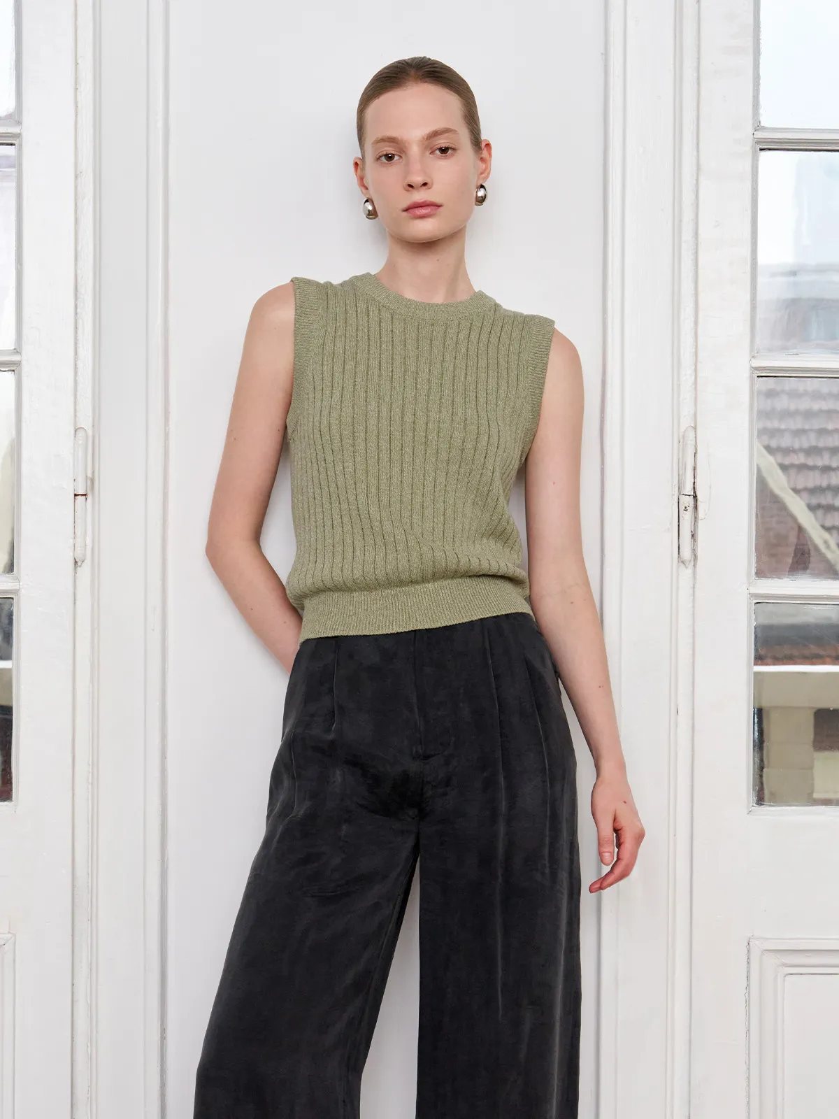 Front-facing model in sage MILLIE tank top with black wide-leg trousers, hands in pockets — confident minimalist style