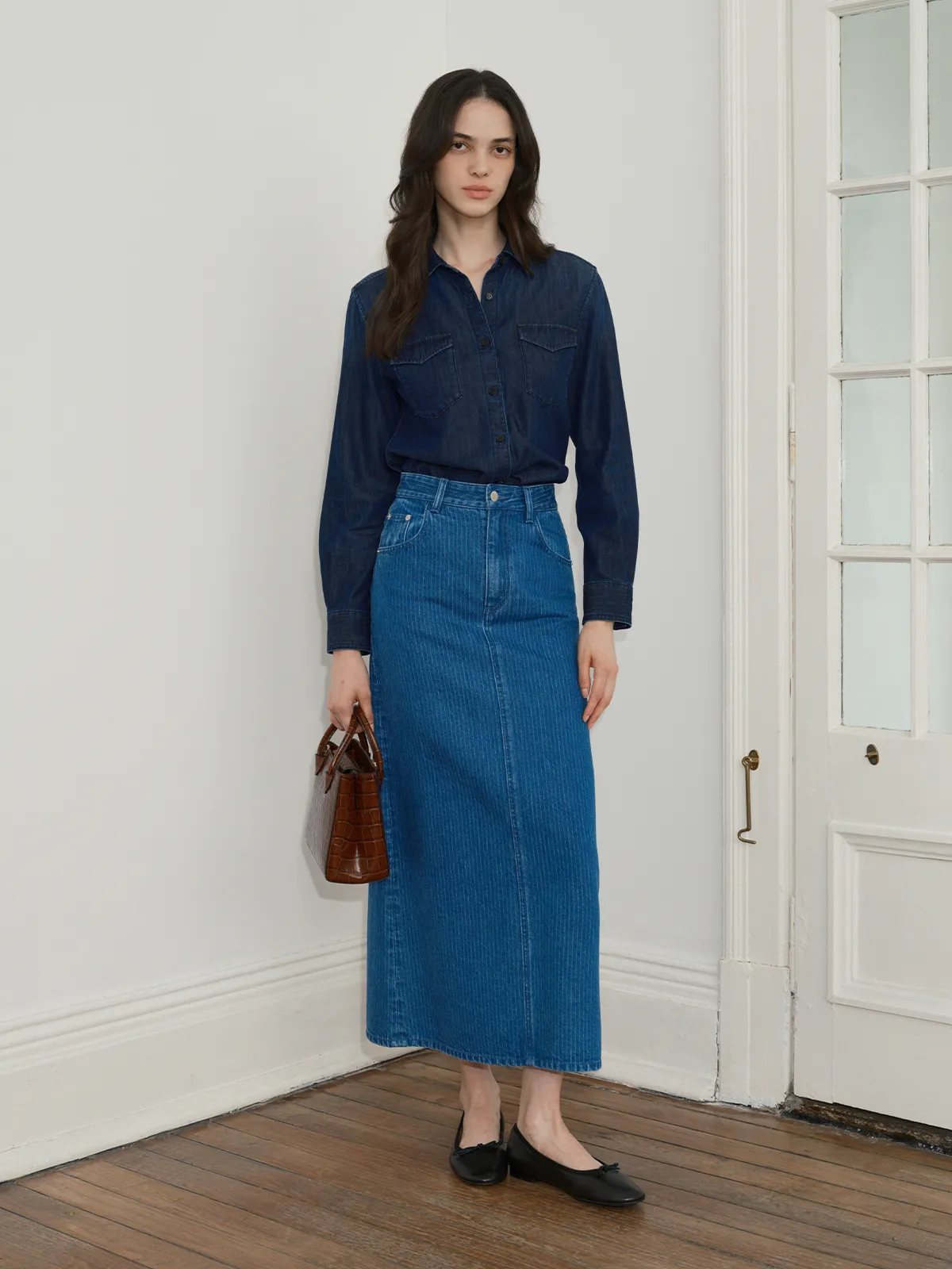 Full front view of model wearing BRYCE striped denim maxi skirt, denim shirt, black ballet flats, holding croc-embossed mini bag