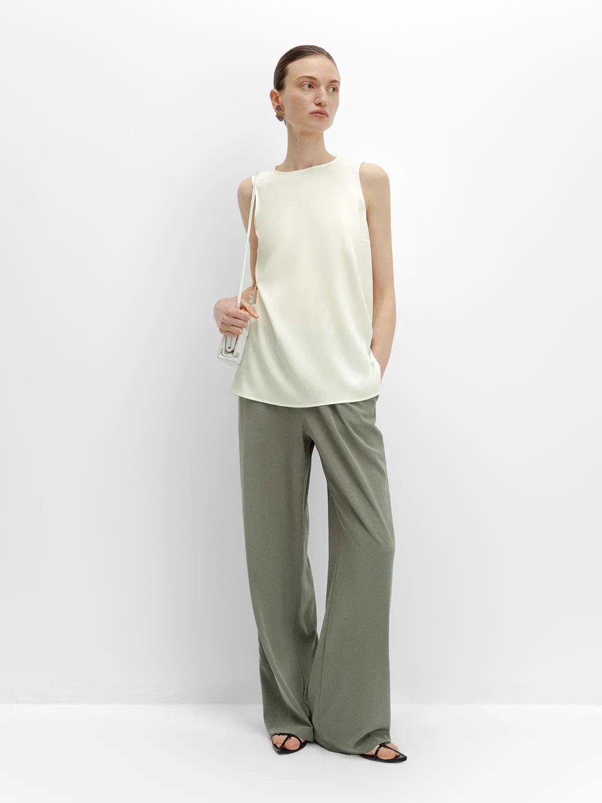 Model in olive green wide-leg pants and ivory MADGE blouse, holding small white shoulder bag, looking off-camera