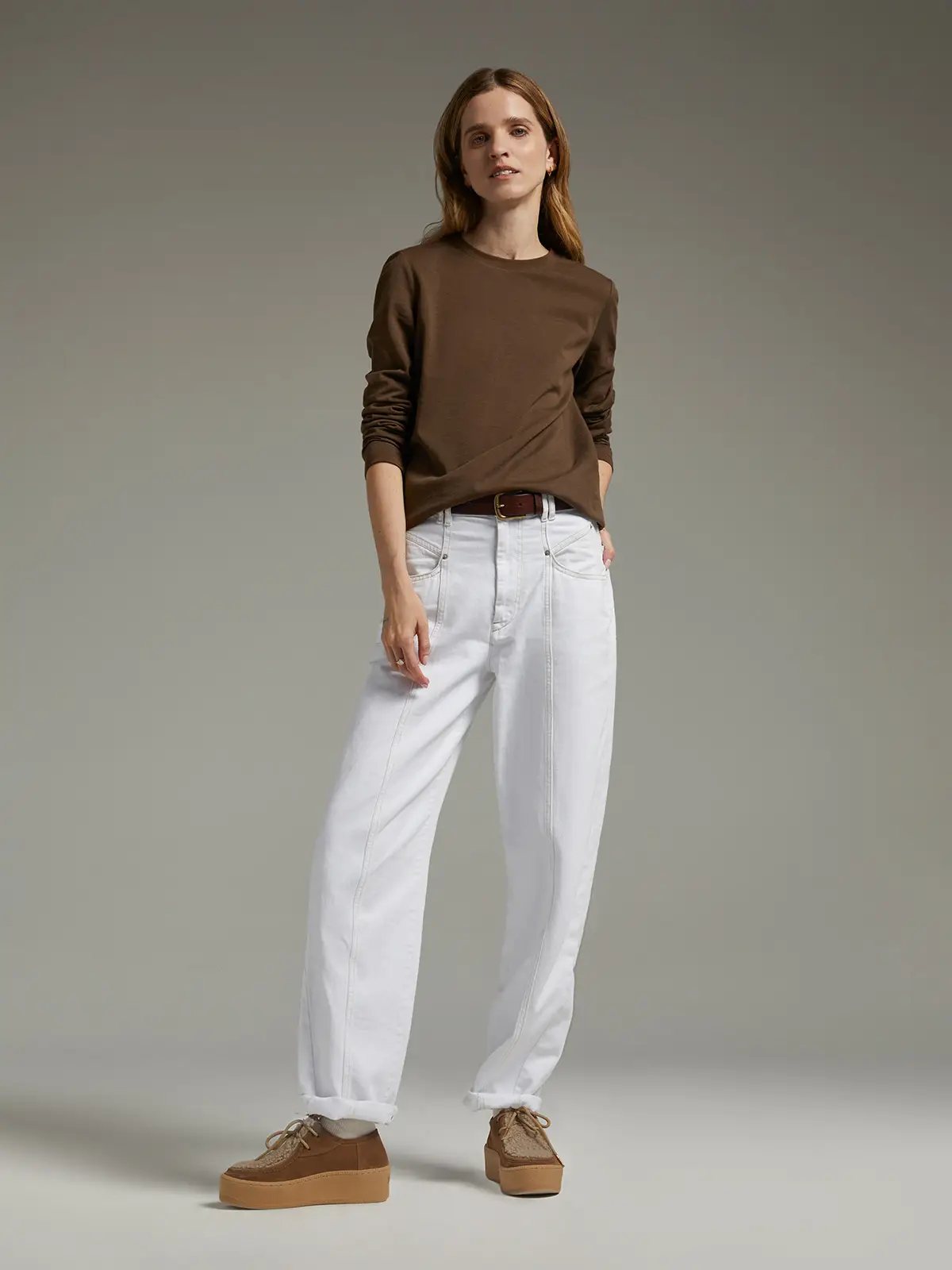 Model wearing a brown long-sleeve crewneck T-shirt tucked into wide-leg jeans with a brown belt and platform shoes.