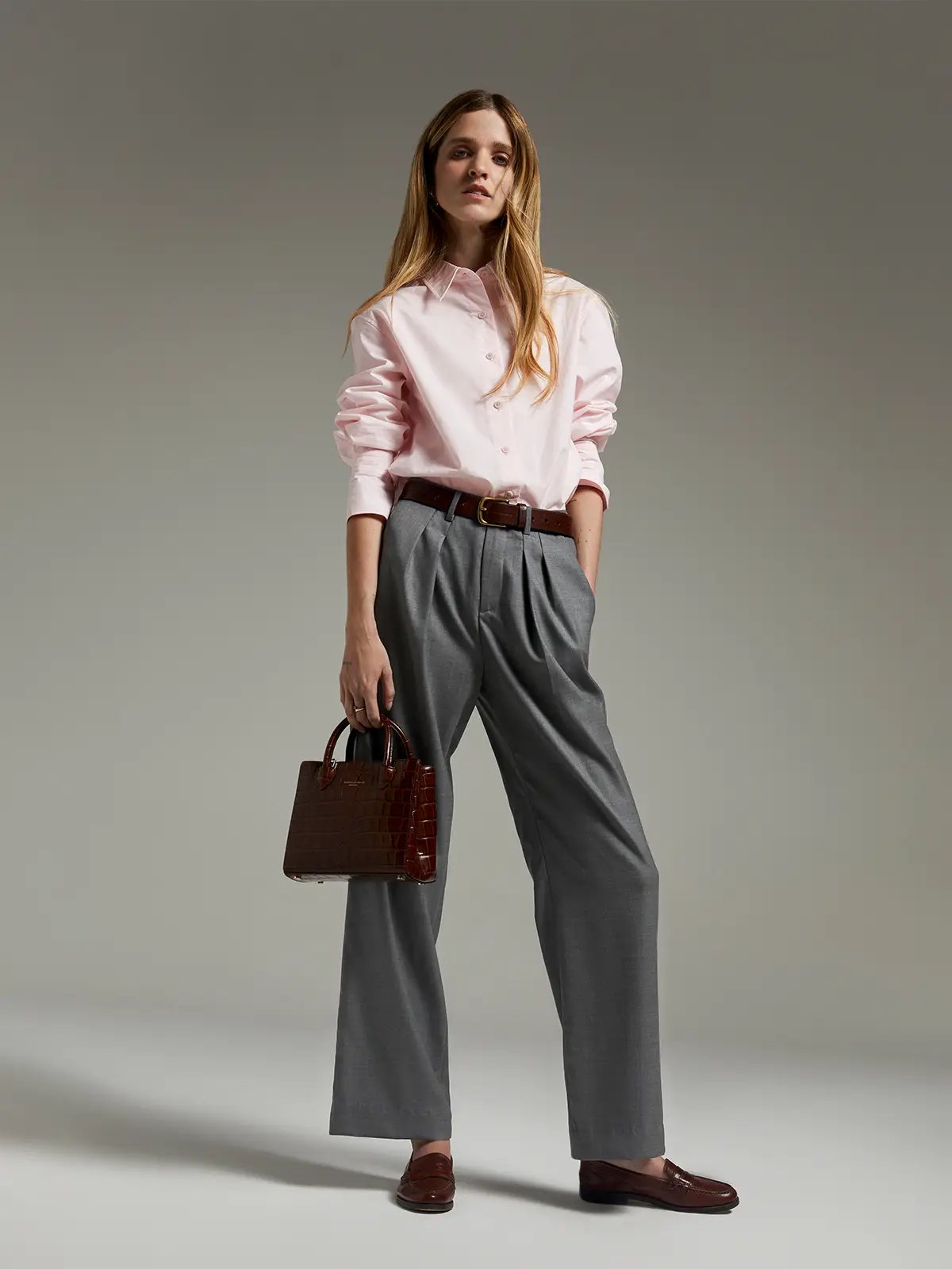 Pink paper-texture cotton shirt tucked into pleated trousers with belt and matching handbag.