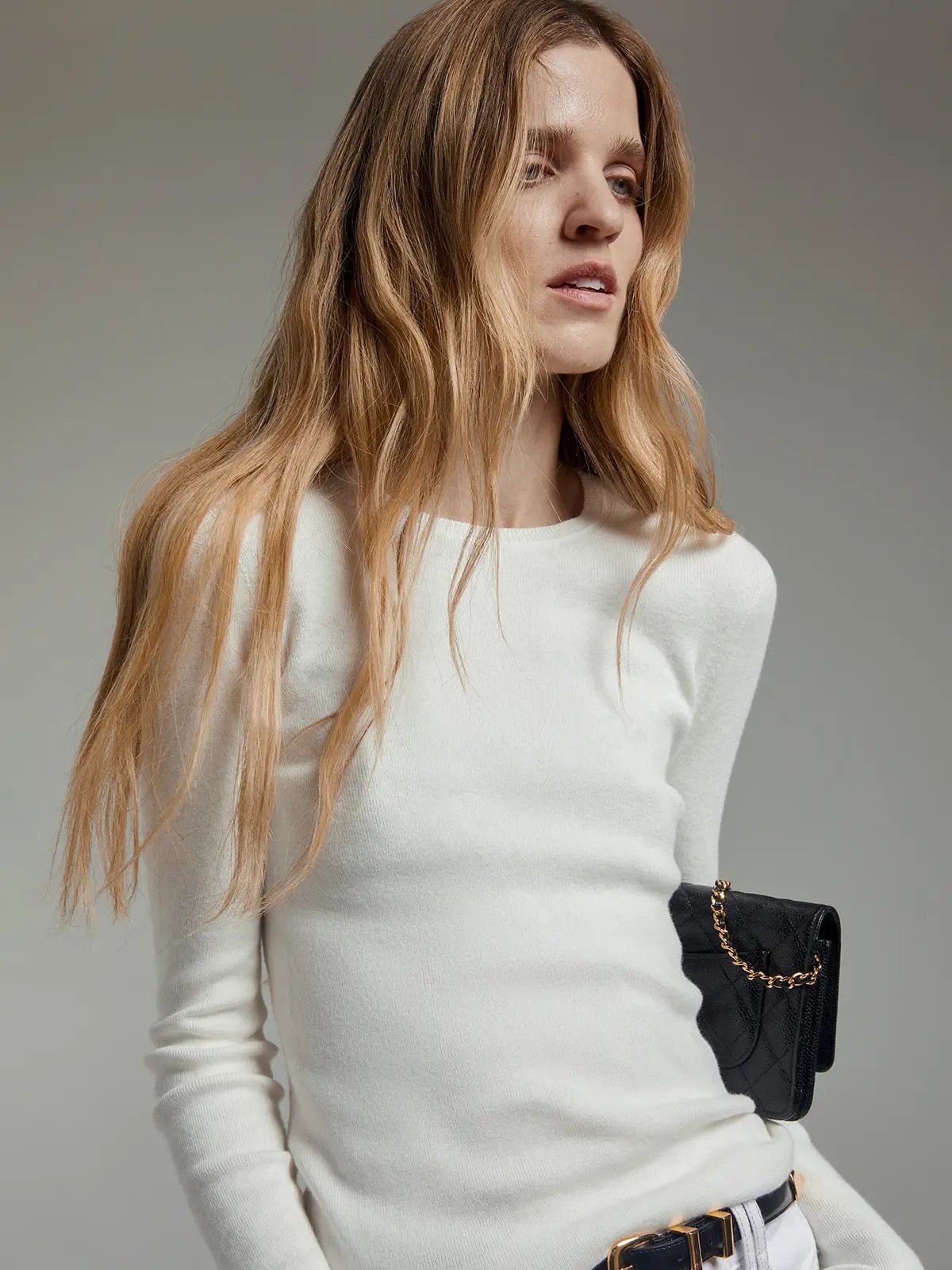 Model in a white slim fit long-sleeve knit top with crew neck, holding a chain-strap bag.