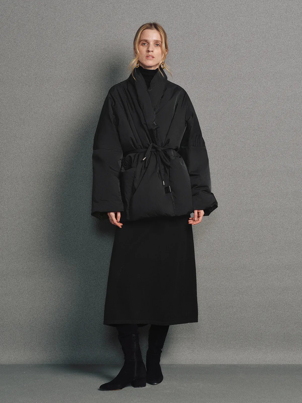 Model wears the Black OPHELIA relaxed wrap-style down coat with wide sleeves, tied waist, and hands in pockets.