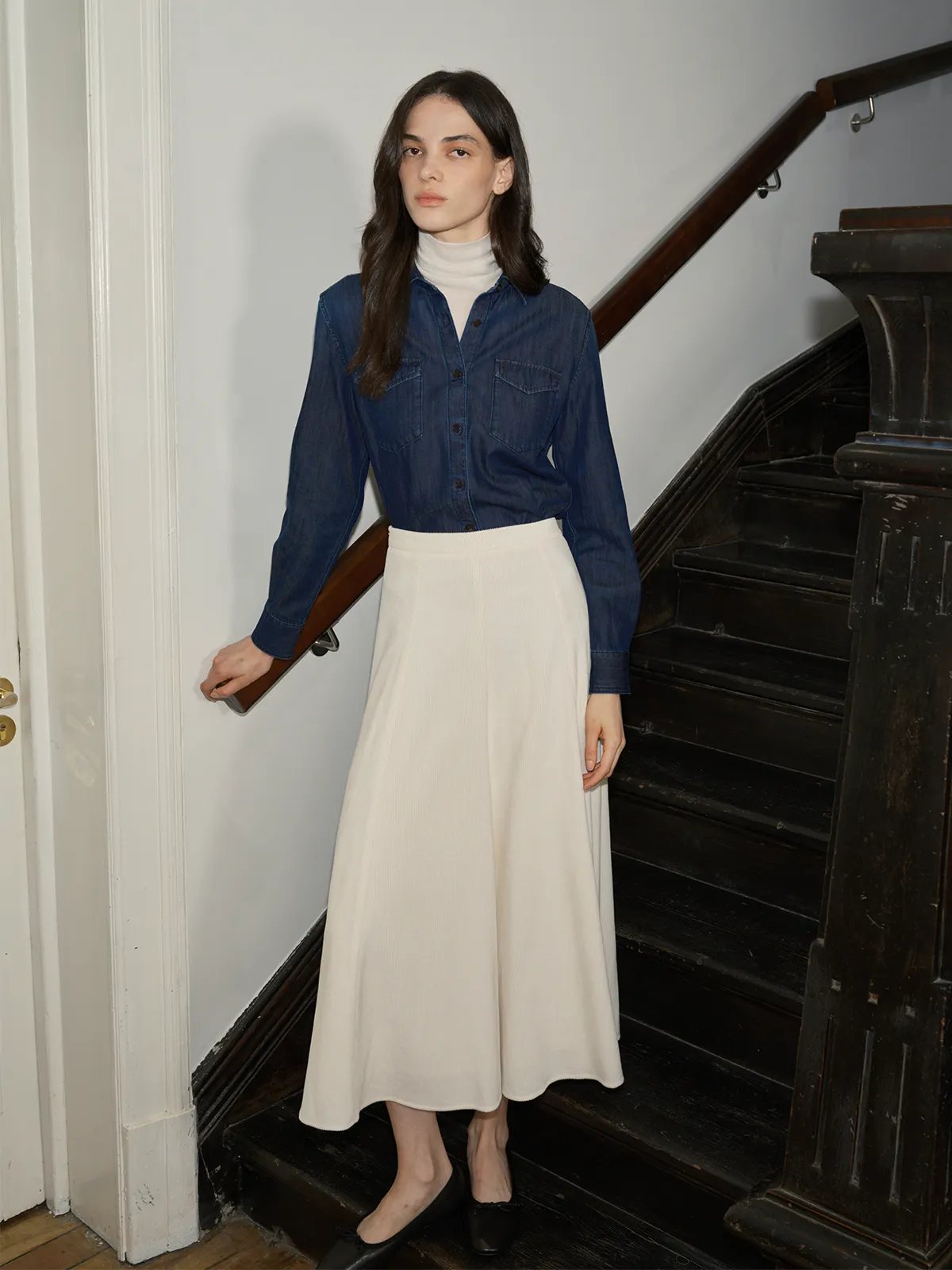 Model on staircase wearing MILIAN maxi skirt with denim shirt over white turtleneck and black flats
