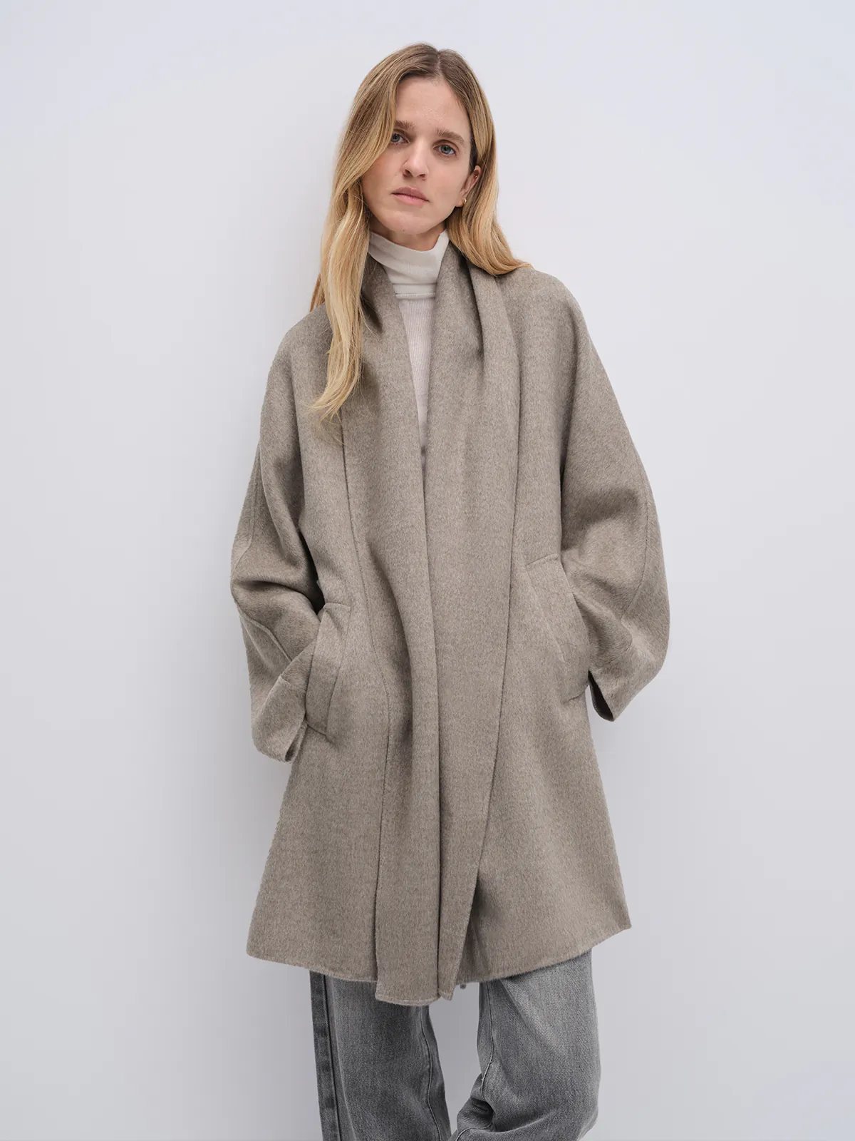 Side view of the Taupe yak wool robe coat with arms crossed, highlighting its drape, length, and voluminous sleeves.