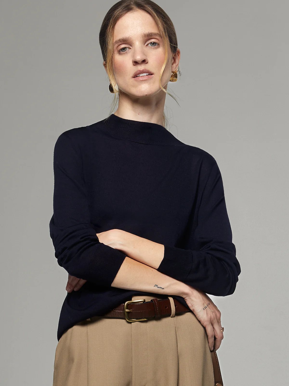 Front view of a model in a navy silk lyocell mock-neck top with long sleeves, tucked into trousers with a belt.