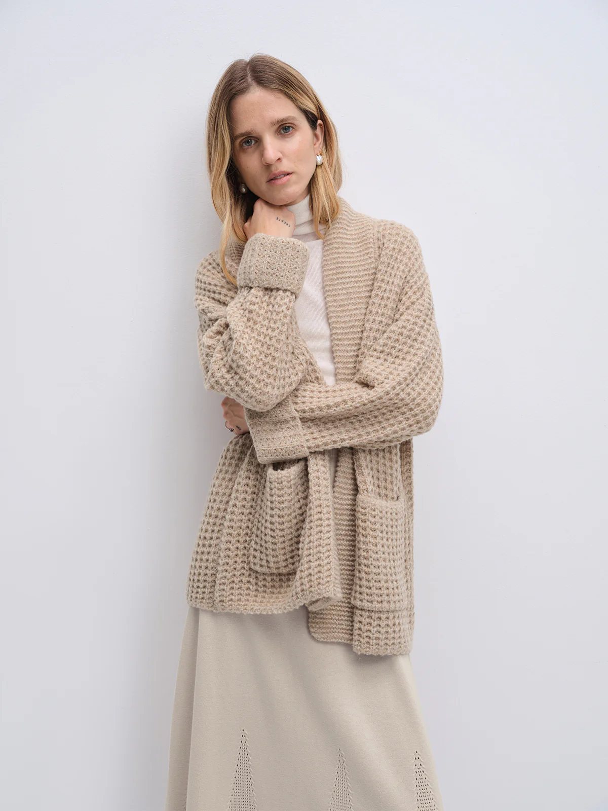 Model wearing the Apricot textured knit cardigan with arms crossed over a turtleneck and skirt.