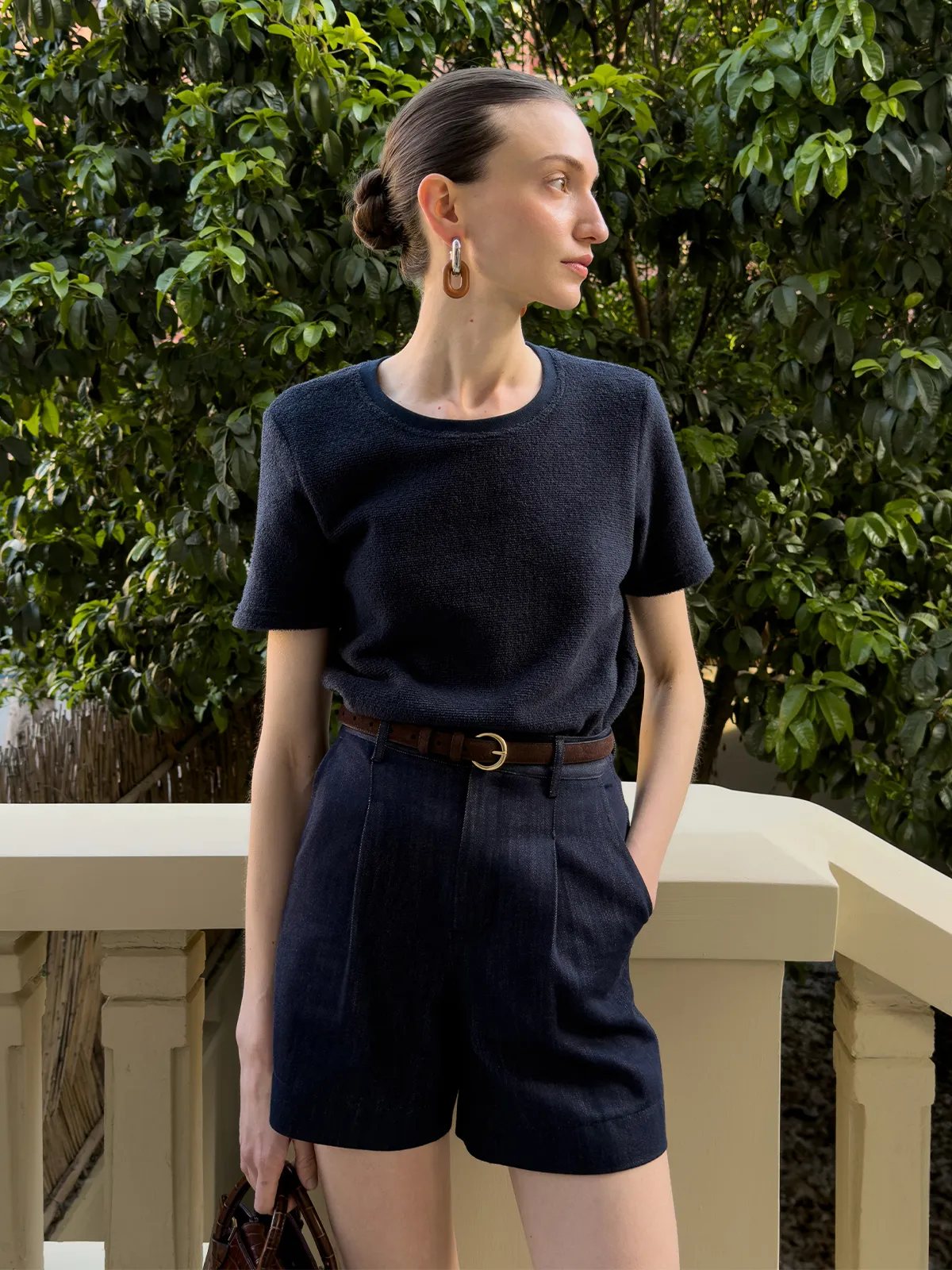 Model wearing RANGER suede belt outdoors with green foliage backdrop, navy knit top and pleated shorts