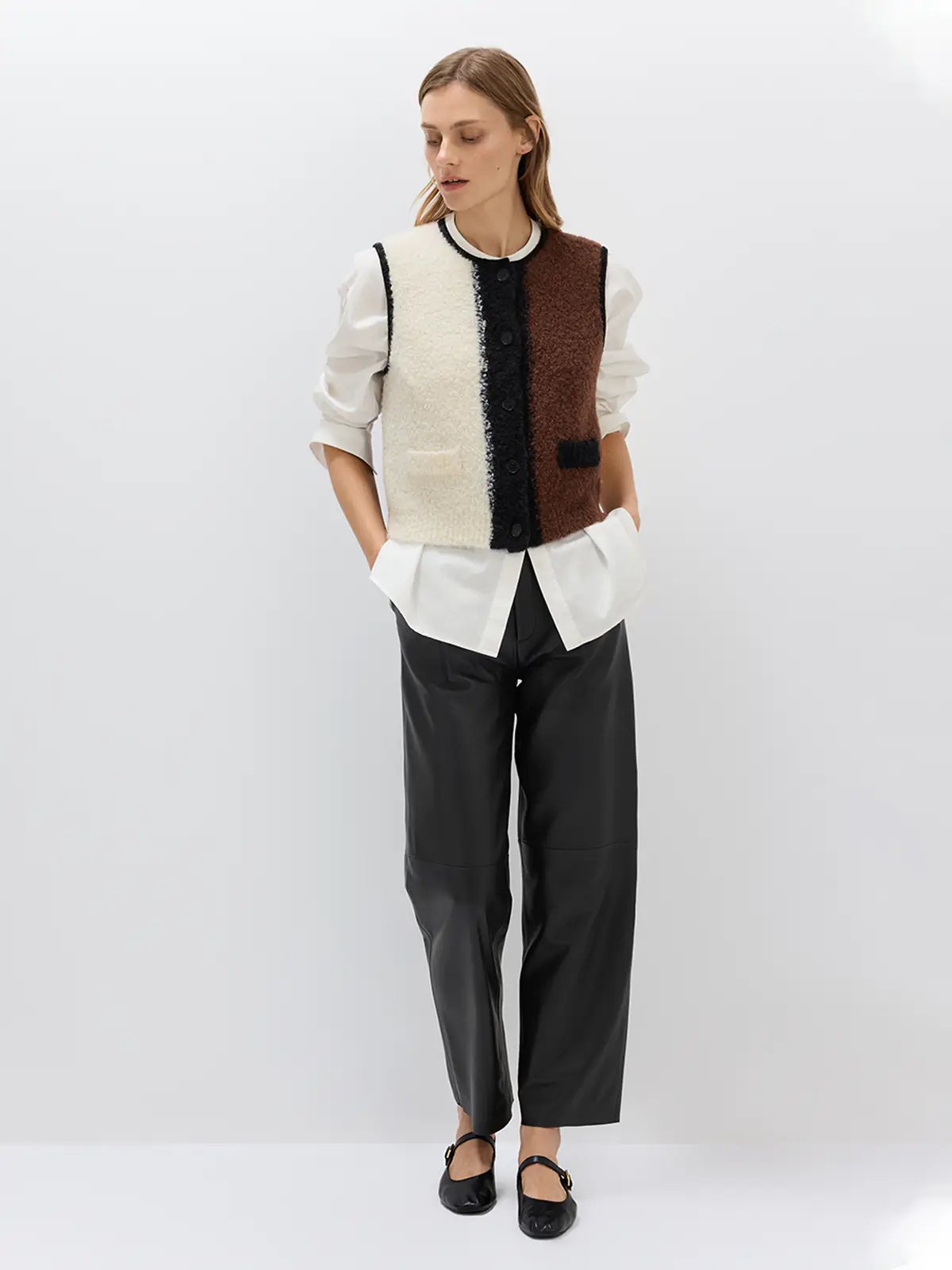 Close-up of the Brown/White/Black colorblock knitted vest showing textured panels, black buttons, and contrast trim at the neckline and armholes.