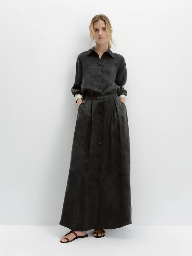 Model wearing black NOBU Maxi Skirt with matching shirt, hands in pockets, minimalist white background
