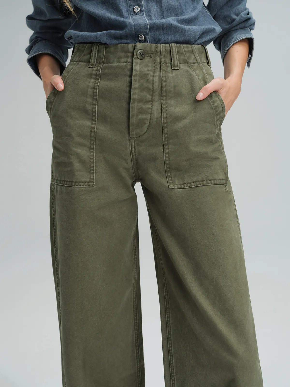 Side view of olive green cotton utility trousers showing wide-leg cut, front pockets, and belt loops.