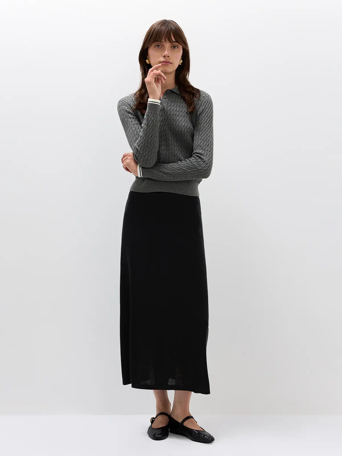 Front view of model in a Grey cable knit polo with long sleeves, ribbed cuffs, and a collar, styled with a denim skirt and bag.