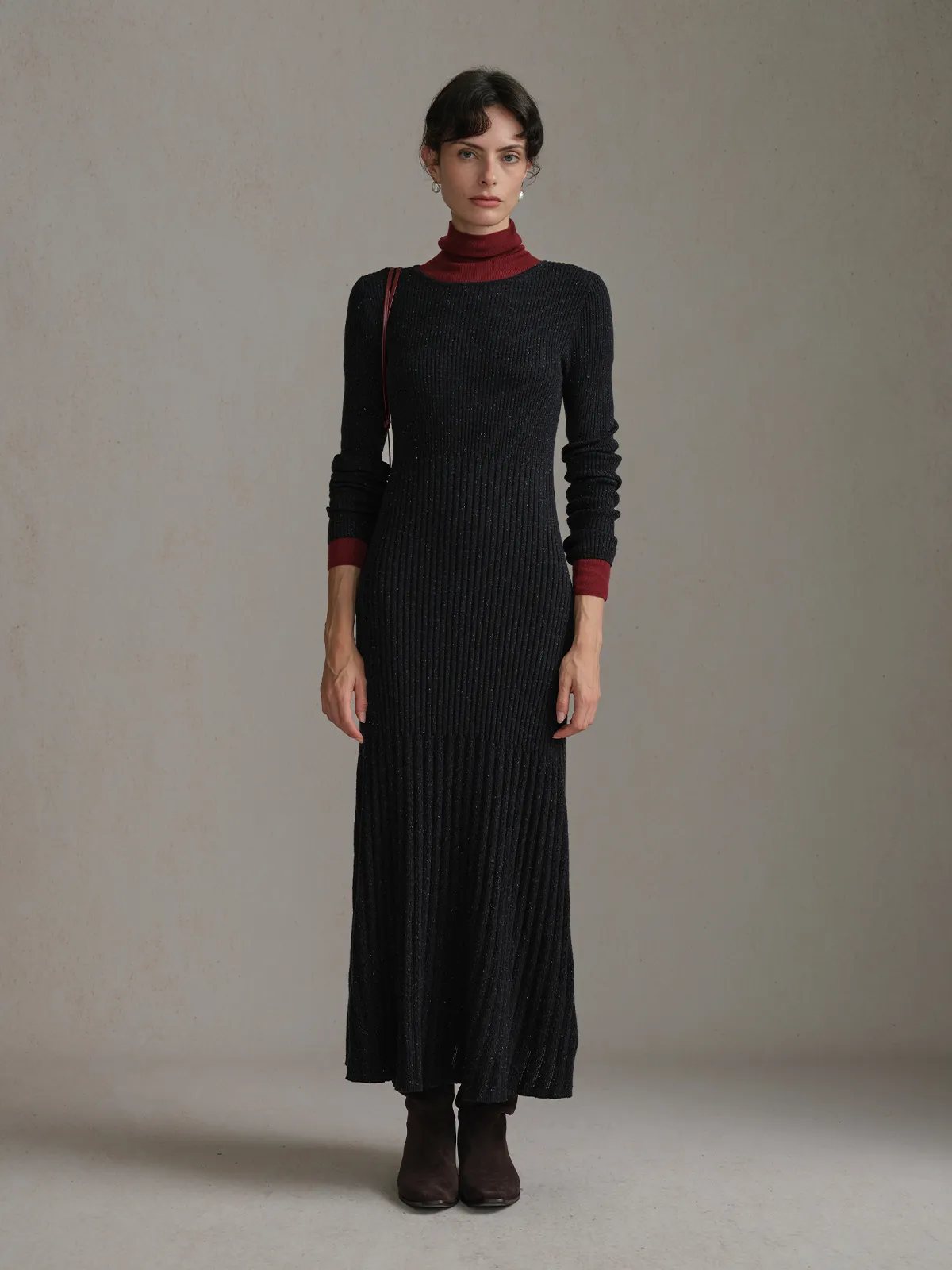 Full-body front view of model wearing black BRENDA maxi dress layered over burgundy turtleneck with brown ankle boots
