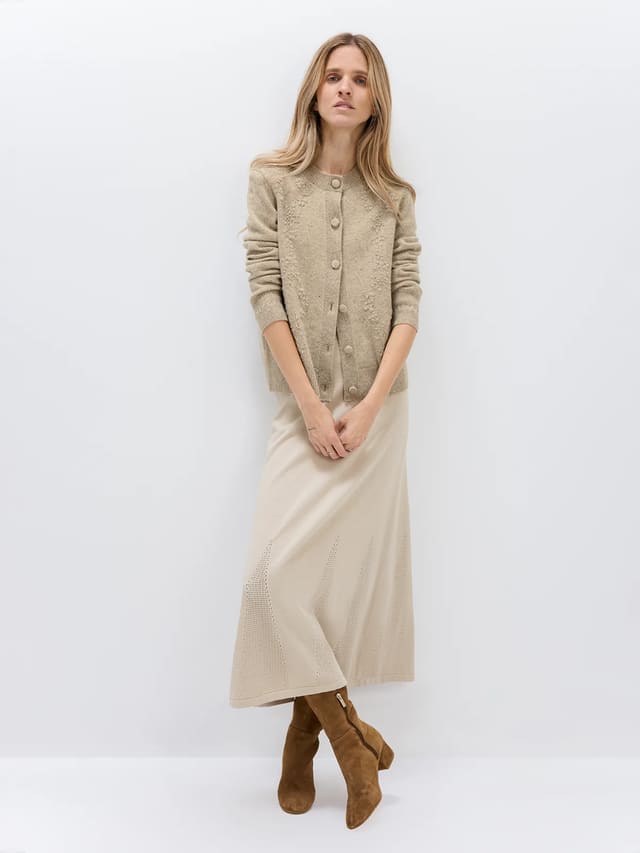 Model wearing a Light Brown Donegal knit cardigan with floral texture, button front, and ribbed cuffs, paired with a light skirt.