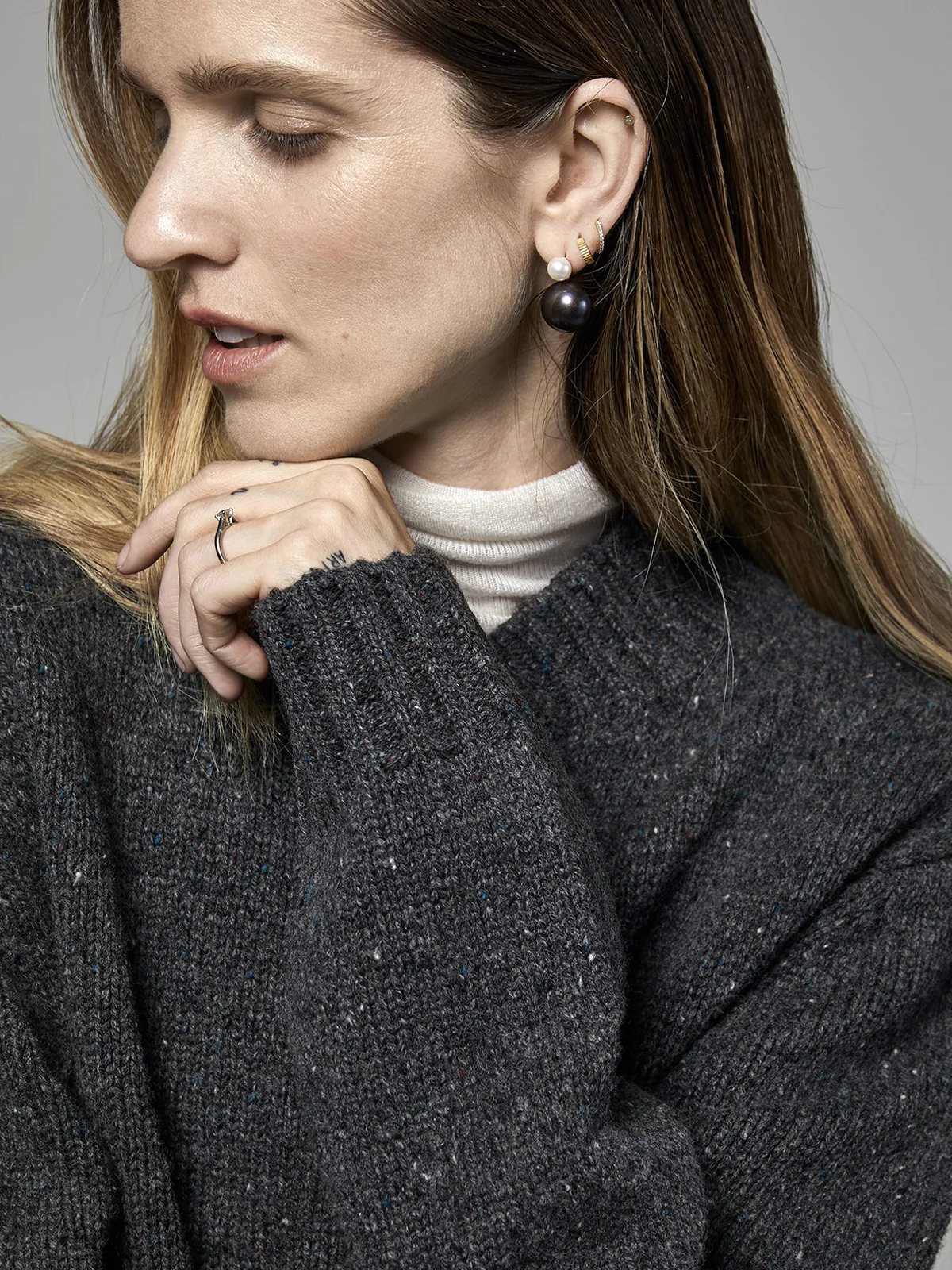 Side view of the Dark Gray Merino Wool Baseball Cardigan worn over a turtleneck, model with hand on hip.