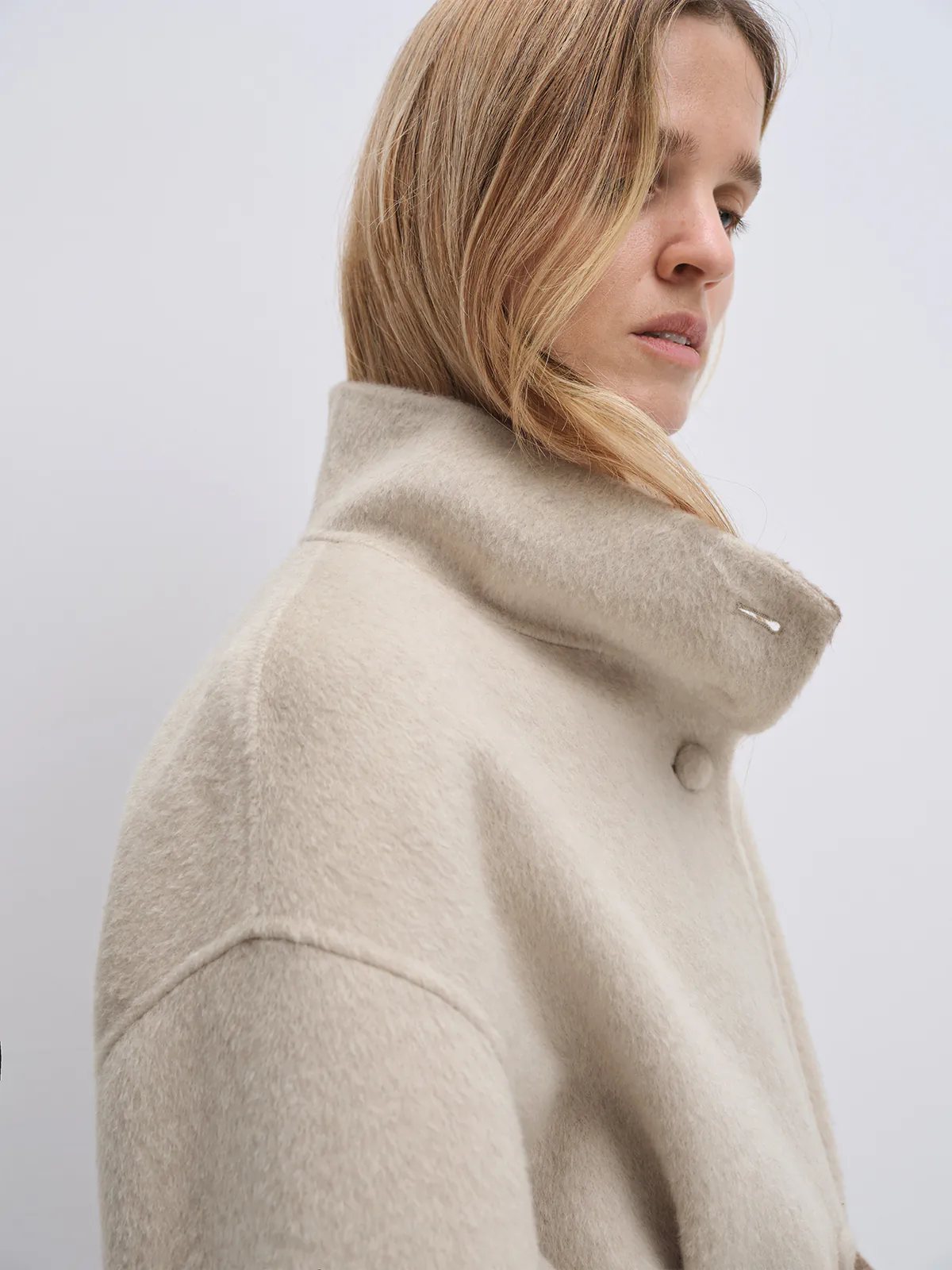Model wearing the Oatmeal reversible two-tone long coat with belt tied, front-facing with hands in pockets.