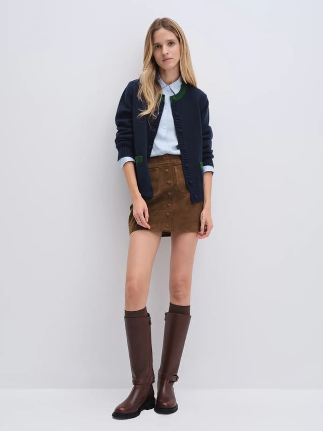 Model wearing navy cardigan with contrast trim at collar and patch pockets, paired with light shirt and skirt.