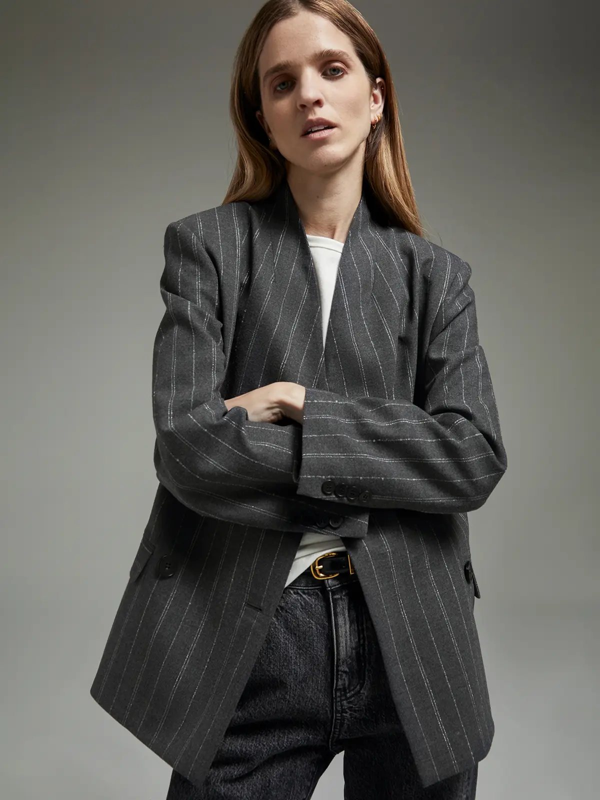 Close-up of model with arms crossed, wearing a gray blazer with vertical stripes over a top.