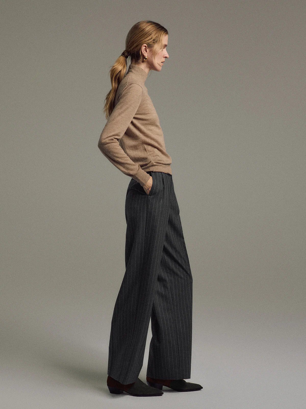 Model in Dark Gray wool striped wide-leg trousers standing in side profile with hands in pockets.