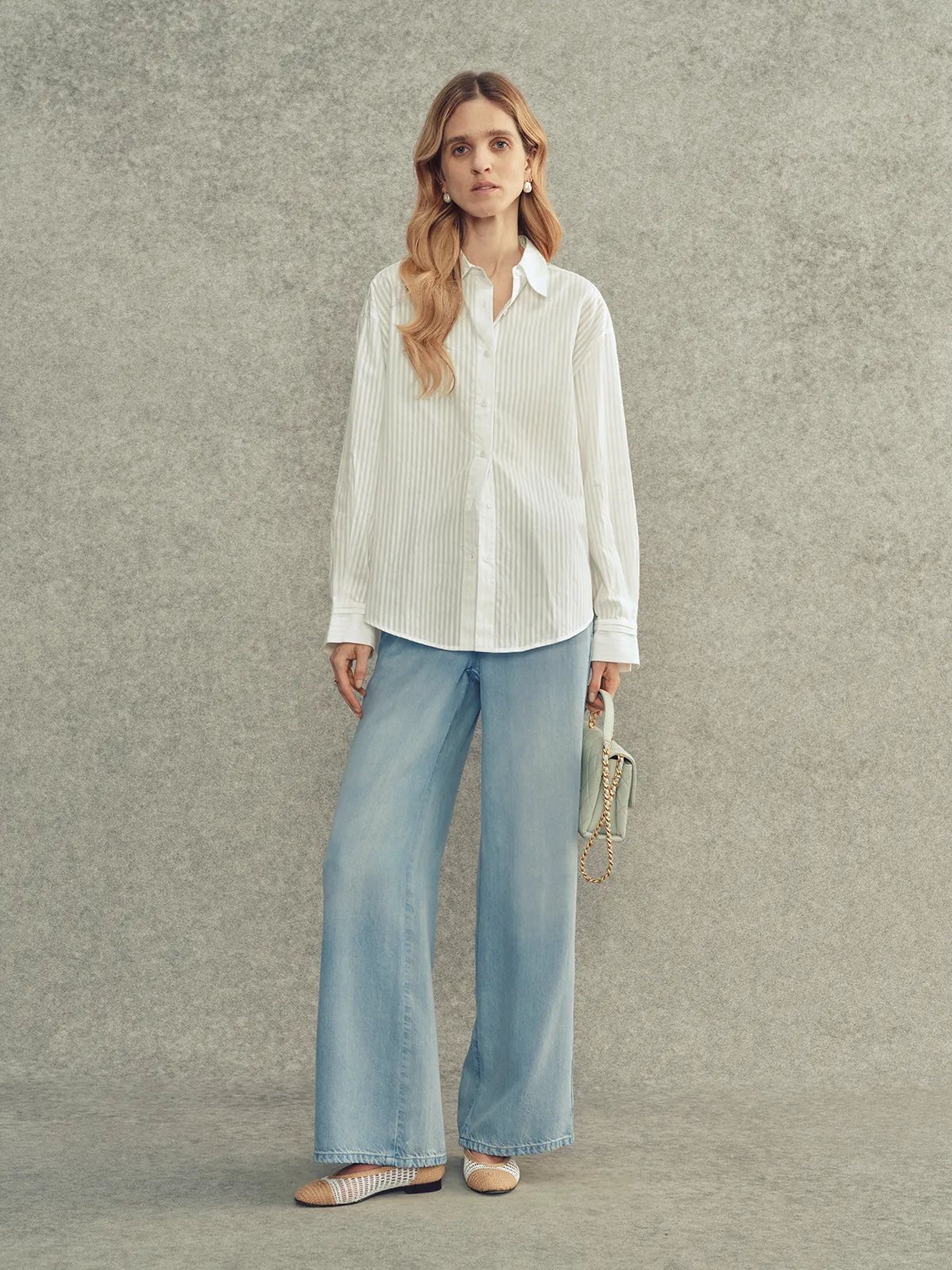 Model wearing LEANNE wide leg jeans with ivory striped shirt, mint quilted bag, and woven flats against gray backdrop