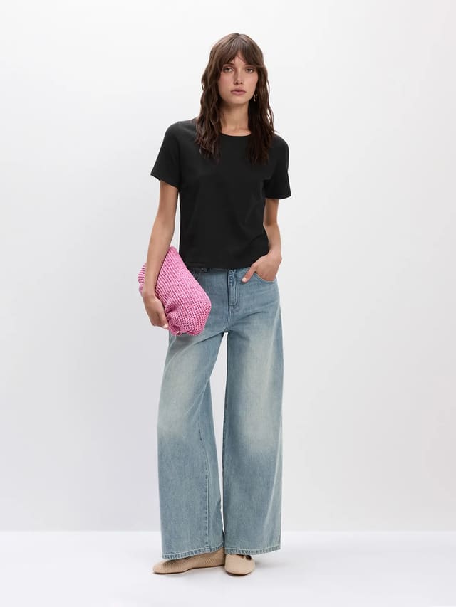 Model wearing black SOSA classic short sleeve t-shirt with wide-leg jeans and pink clutch, quiet luxury street style