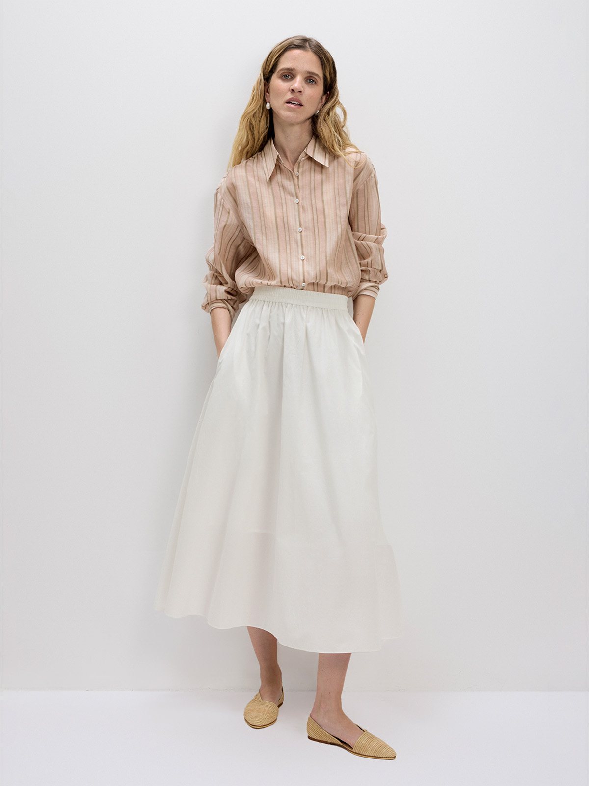 Ivory maxi skirt with beige striped shirt and raffia flats, full-body front pose against white wall