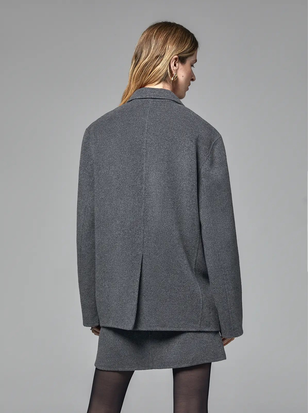 Back view of a Mixed Gray merino wool blazer showing center vent and clean tailoring, worn with matching skirt and tights.