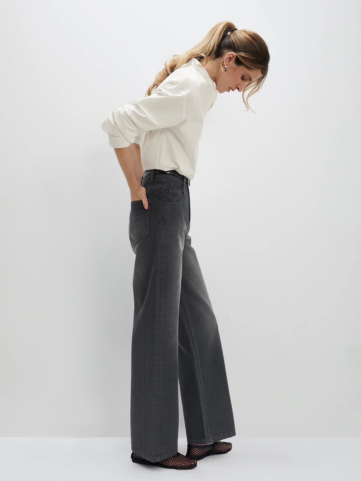 Side view of model wearing gray wide-leg jeans with blouse and mesh flats.