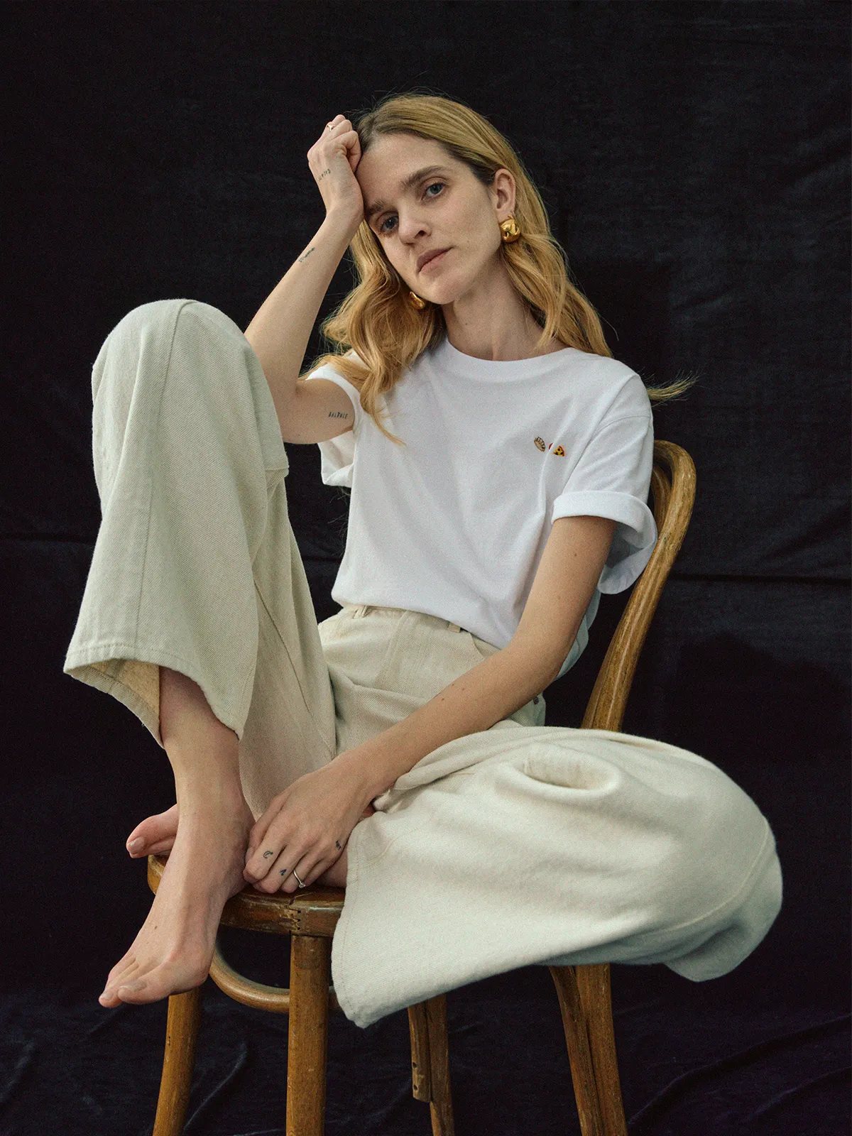 Model seated on wooden chair wearing white Lover's T-Shirt with relaxed wide-leg pants