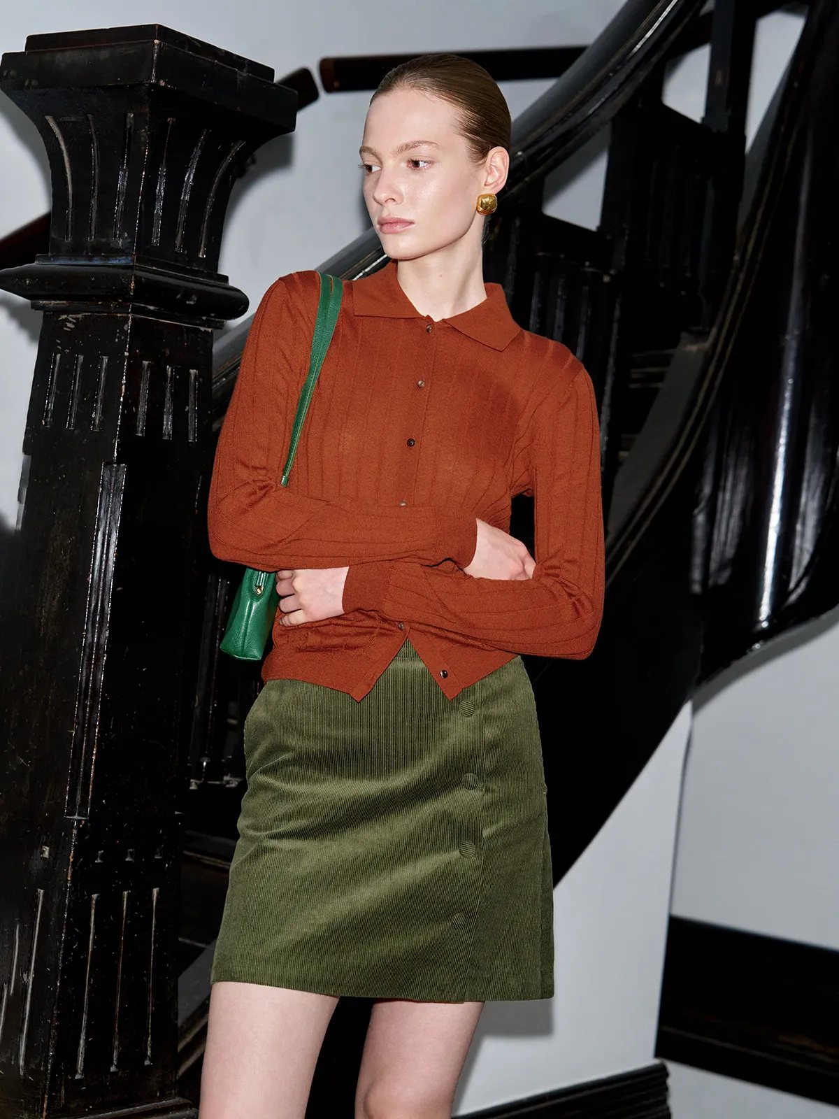 Model in YUKI skirt with rust knit cardigan and green leather bag on ornate staircase