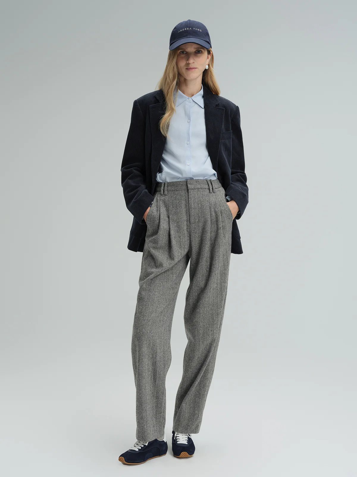 Front view of the navy corduroy tailored blazer worn over a light shirt with pleated trousers and sneakers.