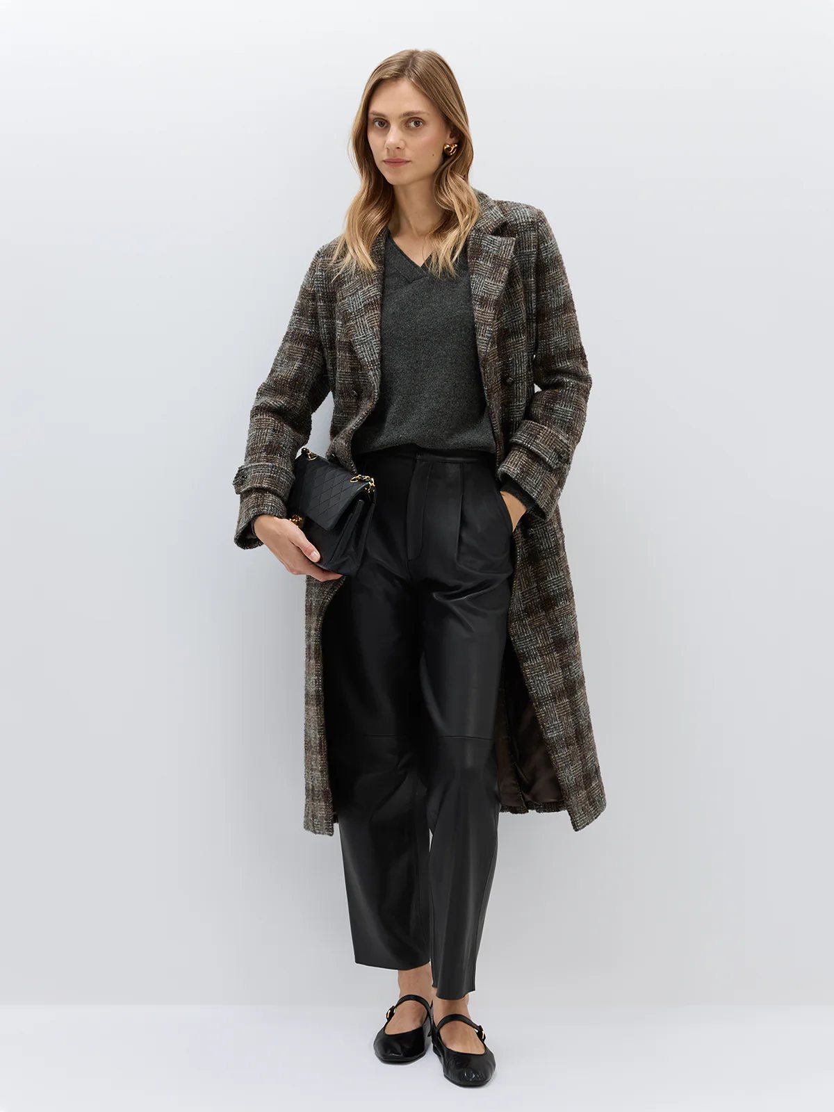 Model wearing the Dark Brown wool alpaca tweed check coat open over a dark sweater and leather pants, holding a bag.